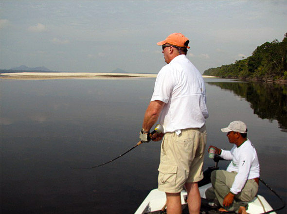 Nick Owings rips his woodchopper topwater nears sandbars far up the Rio Negro with low mountains and ancient volcanoes in the distance while expert river peacock bass guide G advises.